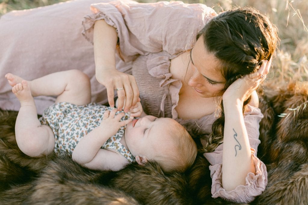 Mother and daughter laying on blanket while mother plays with her hands.