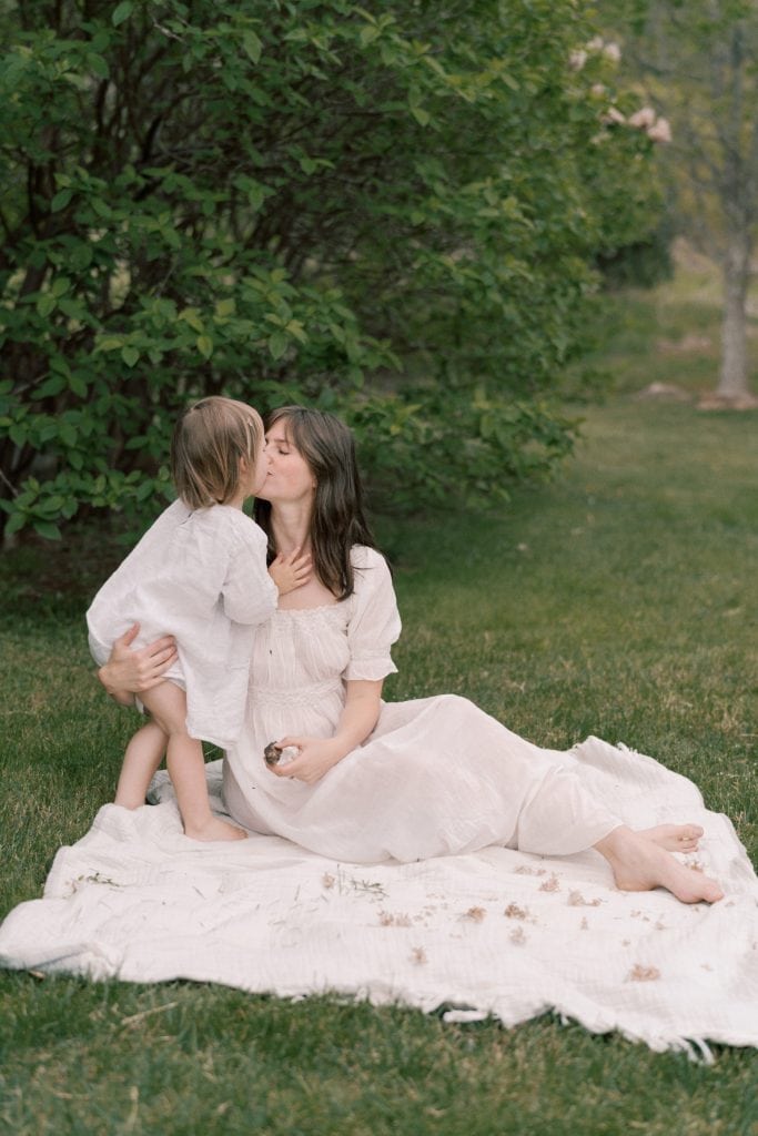 Little girl kissing mom while she's sitting on a blanket.