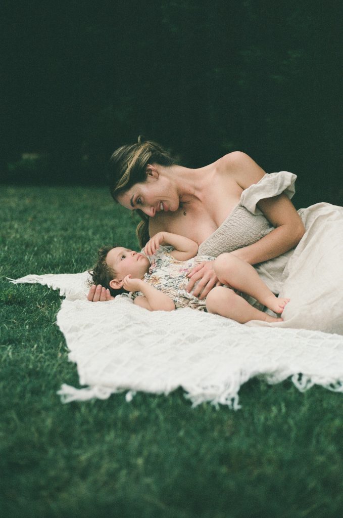 Mother and daughter laying on blanket while mother is looking down on daughter.