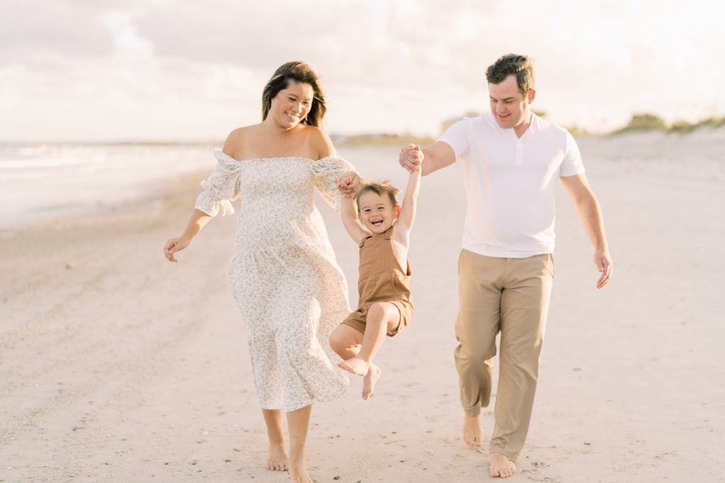 Family of three walking on the beach while swinging their son during their beach photos in Jacksonville, fl.