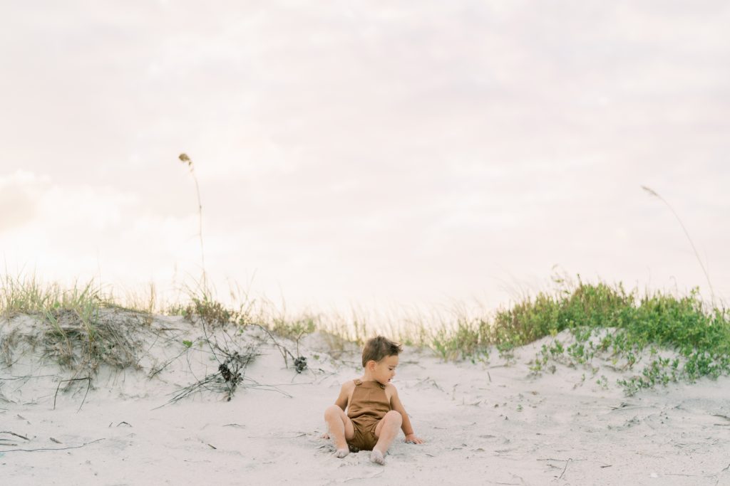 Little boy sitting on the beach during his family beach photography session.