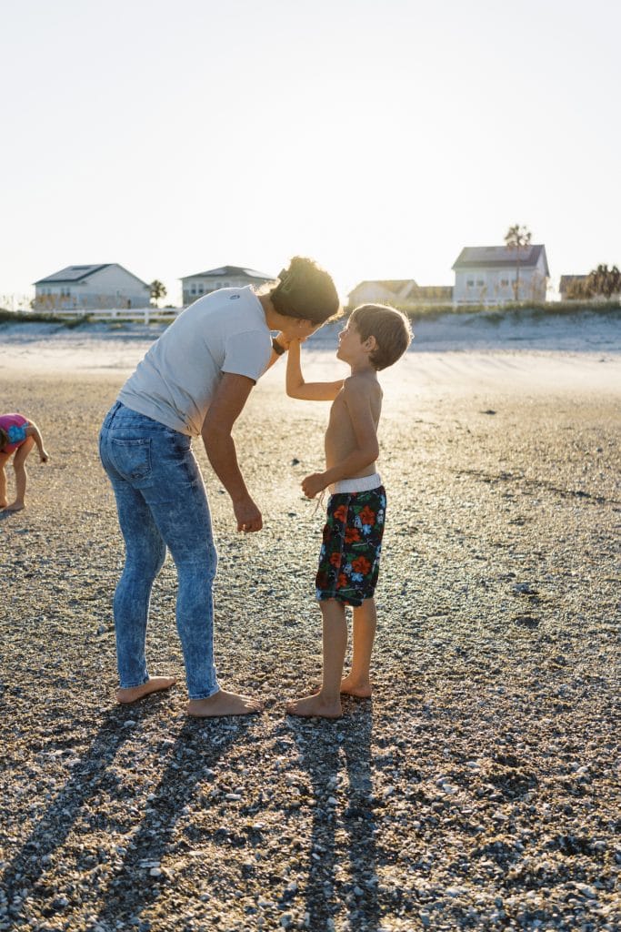 Family documentary photographer, boy holding up shell to mother's ears at the beach.